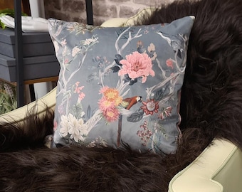 May include: A gray velvet pillow with a floral and bird print. The pillow features pink flowers, green leaves, and a small orange bird.