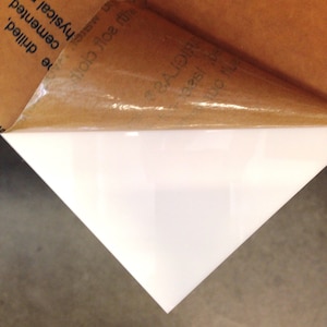 May include: A white sheet of acrylic plastic with a brown protective film partially peeled off.