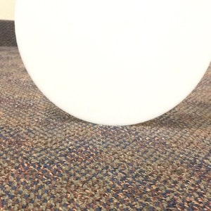 May include: A close-up of a white round object on a patterned carpet. The carpet has a brown, blue, and beige pattern.