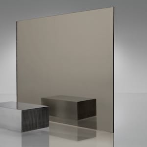 May include: A large sheet of reflective, dark brown tinted glass. The glass is standing upright on a white surface. Two rectangular blocks of metal are in front of the glass.