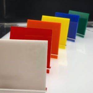 May include: A set of seven acrylic sheets in various colors, including white, red, orange, yellow, blue, green, and a dark green. The sheets are arranged in a row, with the white sheet at the front and the dark green sheet at the back.