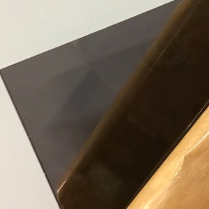 May include: A close-up of a dark gray, rectangular piece of glass being held by a wooden tool.