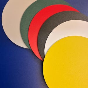 May include: A collection of colorful, circular paper cutouts in various shades, including beige, green, red, black, white, and yellow. The cutouts are arranged in a fan shape against a blue background, showcasing their diverse hues and textures.