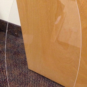 May include: A clear, oval-shaped piece of transparent plastic or glass, possibly a protective cover or decorative element. The object is positioned against a wooden surface and a patterned carpet.