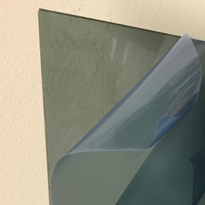 May include: A sheet of clear acrylic plastic with a protective film on one side. The film is partially peeled back to reveal the clear acrylic underneath.