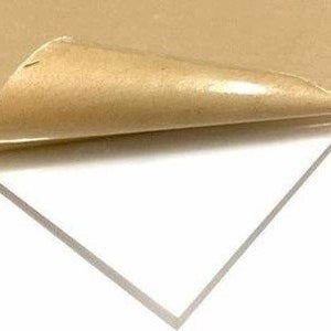 May include: A clear acrylic sheet with a protective brown paper backing. The paper is partially peeled back to reveal the smooth, transparent surface of the acrylic.