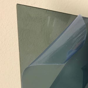 May include: A sheet of clear acrylic plastic with a protective film on one side. The film is partially peeled back to reveal the clear acrylic underneath.