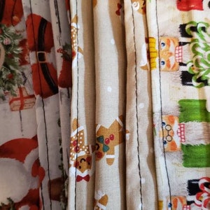 May include: Set of three fabric face masks with Christmas-themed prints. The masks are beige with gingerbread men, white with Santa Claus, and white with a nutcracker.
