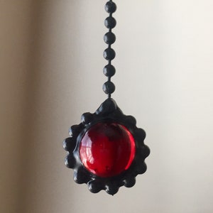 May include: A black chain with a red glass orb pendant. The orb is surrounded by a black metal frame.