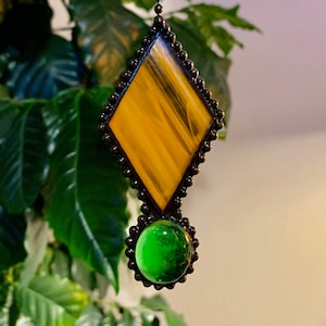 May include: A stained glass suncatcher with a diamond-shaped yellow and orange piece and a round green piece hanging from a chain.