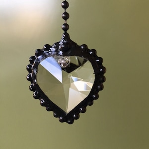 May include: A black chain with a crystal heart-shaped pendant. The heart is faceted and has a black metal frame.