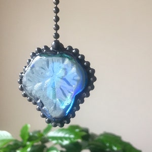 May include: A blue iridescent glass suncatcher with a black metal chain and beaded border. The suncatcher is shaped like a leaf and hangs from a ceiling.