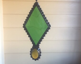 May include: A green diamond-shaped stained glass window hanging from a chain with a small yellow round stained glass piece at the bottom.