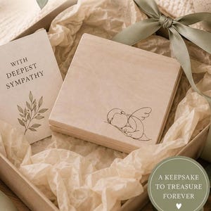 Peut inclure: Un coffret souvenir en bois avec un dessin au trait d'un ange endormi, pr&eacute;sent&eacute; dans une bo&icirc;te cadeau avec une carte indiquant &laquo; AVEC NOS PLUS SINC&Egrave;RES CONDOL&Eacute;ANCES &raquo;. La bo&icirc;te est entour&eacute;e de papier de soie et d'un ruban vert sauge. Un cercle indique &laquo; UN SOUVENIR &Agrave; CH&Eacute;RIR POUR TOUJOURS &raquo;.