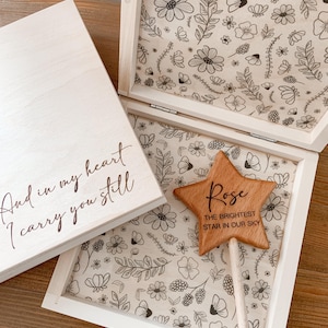 Könnte beinhalten: Eine Holzkiste mit einem Blumenmuster im Inneren. Die Kiste ist geöffnet und ein Holzstern mit dem Text "Rose The Brightest Star In Our Sky" befindet sich darin. Die Kiste hat auch eine handgeschriebene Nachricht auf dem Deckel, die lautet "And in my heart I carry you still."