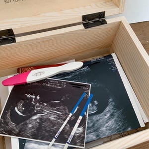 May include: A wooden keepsake box with the text "Baby Was... You were carried for a moment, but you are loved for a lifetime." Inside are ultrasound images, pregnancy tests, and a pink and white pregnancy test.