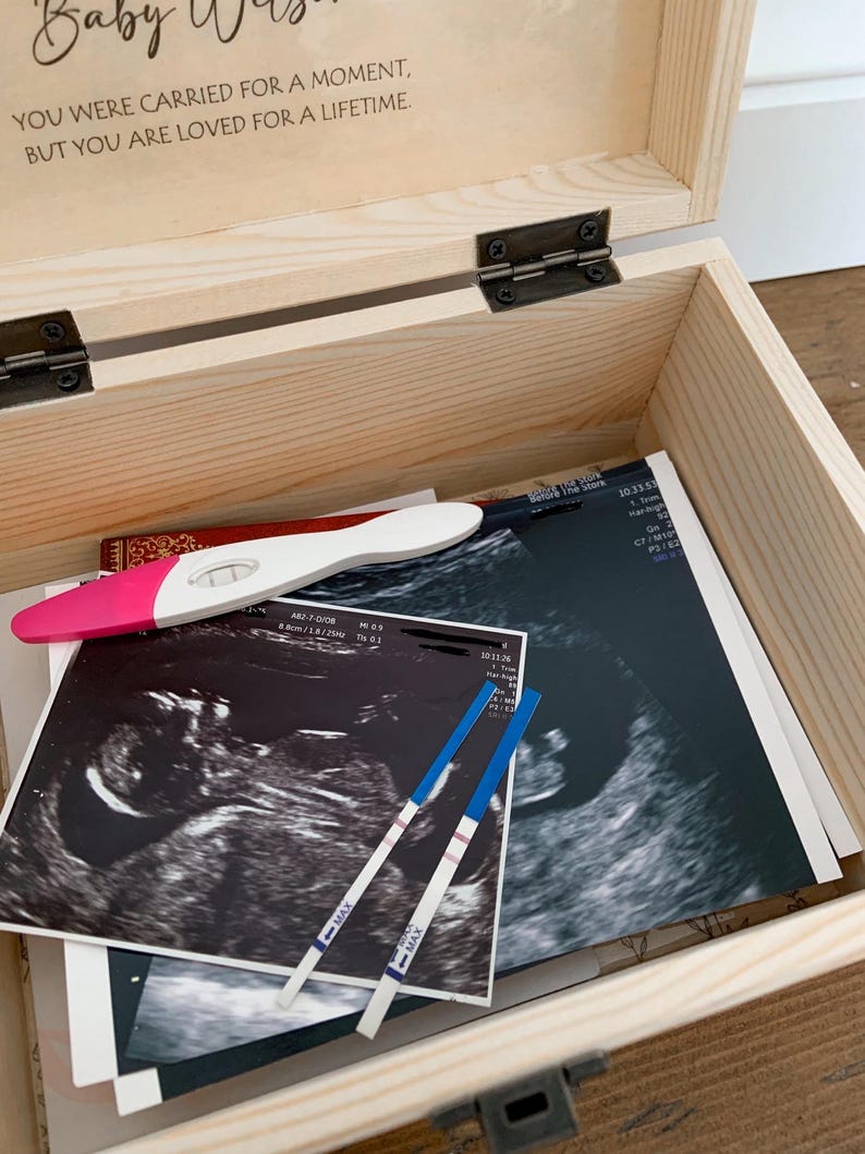 May include: A wooden keepsake box with the text "Baby Was... You were carried for a moment, but you are loved for a lifetime." Inside are ultrasound images, pregnancy tests, and a pink and white pregnancy test.