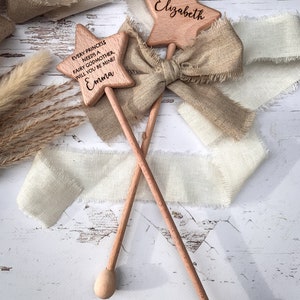 Puede incluir: Dos varitas de madera en forma de estrella con mangos largos y puntas redondeadas. Una varita est&aacute; grabada con el nombre Elizabeth, y la otra presenta el texto: Every princess needs a fairy godmother. Will you be mine! Emma. Una cinta beige deshilachada est&aacute; atada.