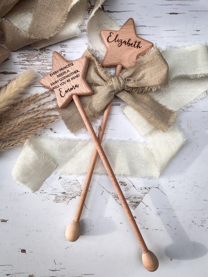 Puede incluir: Dos varitas de madera en forma de estrella con mangos largos y puntas redondeadas. Una varita est&aacute; grabada con el nombre Elizabeth, y la otra presenta el texto: Every princess needs a fairy godmother. Will you be mine! Emma. Una cinta beige deshilachada est&aacute; atada.