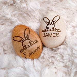 May include: Two wooden Easter eggs with bunny faces and the names "Emma" and "James" engraved on them.