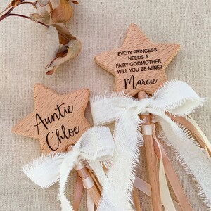Puede incluir: Dos varitas de madera en forma de estrella con veta clara. Una varita est&aacute; grabada con "Auntie Chloe" y la otra con "EVERY PRINCESS NEEDS A FAIRY GODMOTHER. WILL YOU BE MINE?" y "Marcie". Ambas tienen lazos de cinta color crema deshilachados.