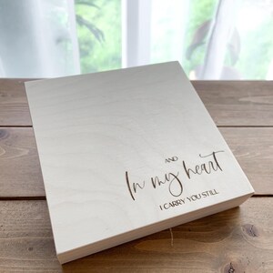 Könnte beinhalten: Helle Holztafel mit den Worten "In my heart" und "I carry you still" in Schreibschrift graviert. Die rechteckige Tafel liegt auf einer Holzoberfläche.