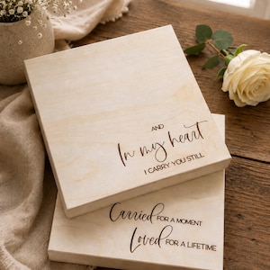 May include: Two square light-coloured wooden plaques with engraved black text. The top plaque reads AND In my heart I CARRY YOU STILL. The bottom plaque reads Carried FOR A MOMENT Loved FOR A LIFETIME. The wood grain is visible on both surfaces.