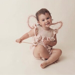 Peut inclure: Un b&eacute;b&eacute; portant une combinaison en tricot rose avec un col &agrave; volants et des ailes en dentelle. Le b&eacute;b&eacute; tient une baguette en bois avec une &eacute;toile &agrave; l'extr&eacute;mit&eacute;.