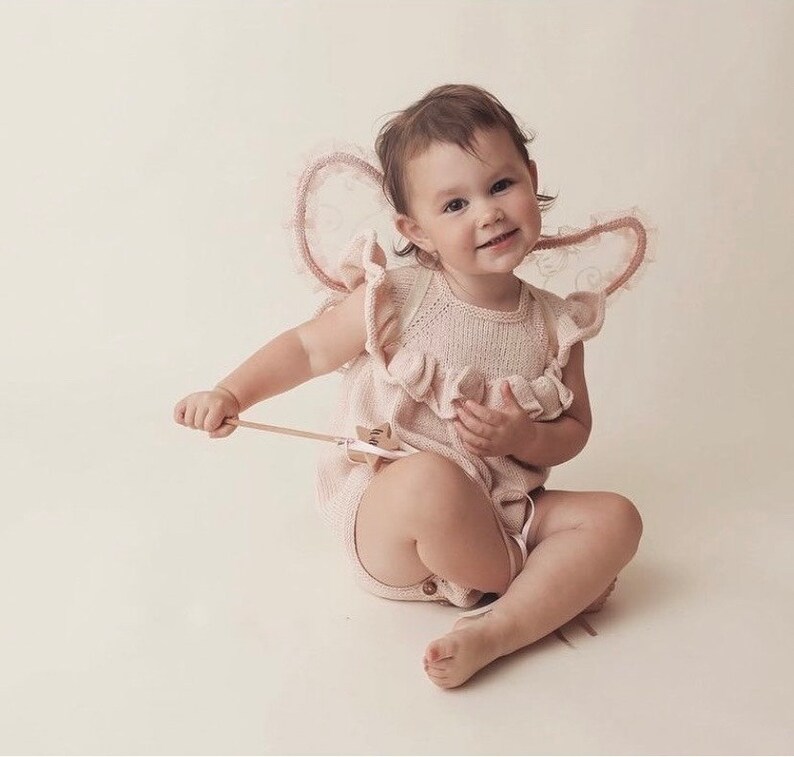 Peut inclure: Un b&eacute;b&eacute; portant une combinaison en tricot rose avec un col &agrave; volants et des ailes en dentelle. Le b&eacute;b&eacute; tient une baguette en bois avec une &eacute;toile &agrave; l'extr&eacute;mit&eacute;.