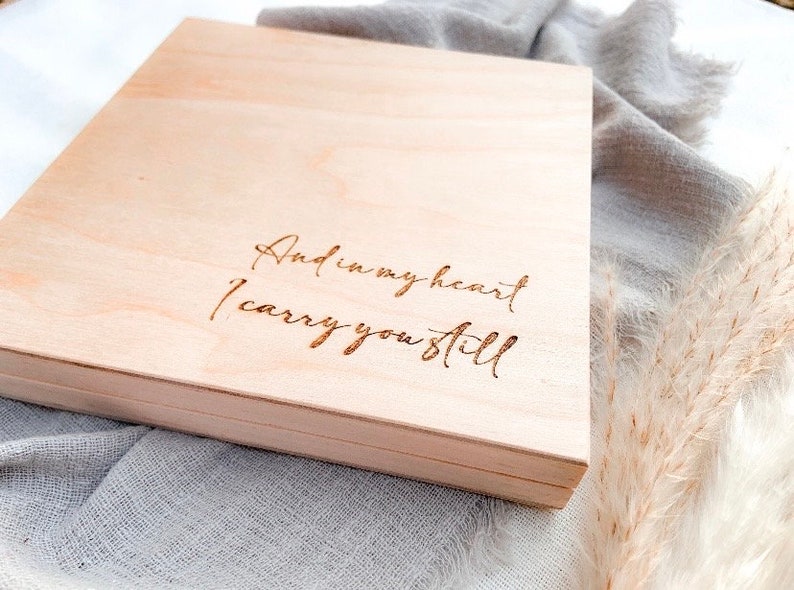 May include: A wooden box with the inscription "And in my heart I carry you still" engraved on the top.