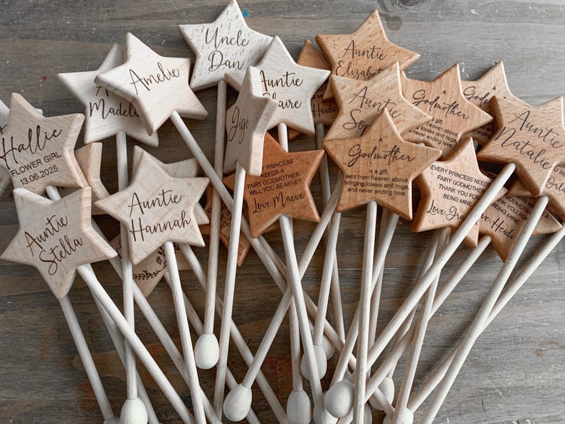 Puede incluir: Una colecci&oacute;n de varitas de madera clara con forma de estrella, cada una unida a un fino palo de madera. Las estrellas est&aacute;n grabadas con varios nombres y t&iacute;tulos como Auntie, Godmother y Flower Girl, junto con breves mensajes personalizados.