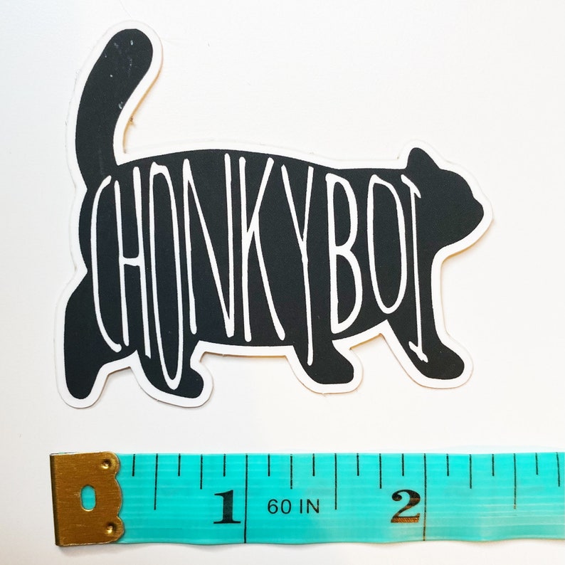 Op de afbeelding: Zwart-witte sticker van een cartoonkat met de tekst "CHONKY BOI" erop. De sticker is ongeveer 5 cm breed.