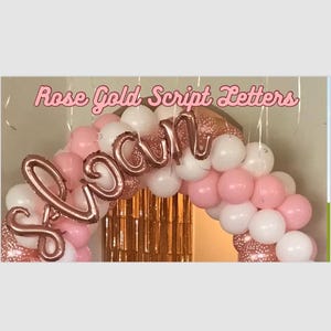 May include: Rose gold script letters spelling "Sloan" in a balloon arch made of pink and white balloons.