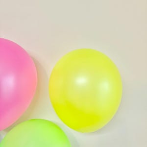 May include: Three balloons in different colours: pink, yellow and green. The balloons are against a white background.