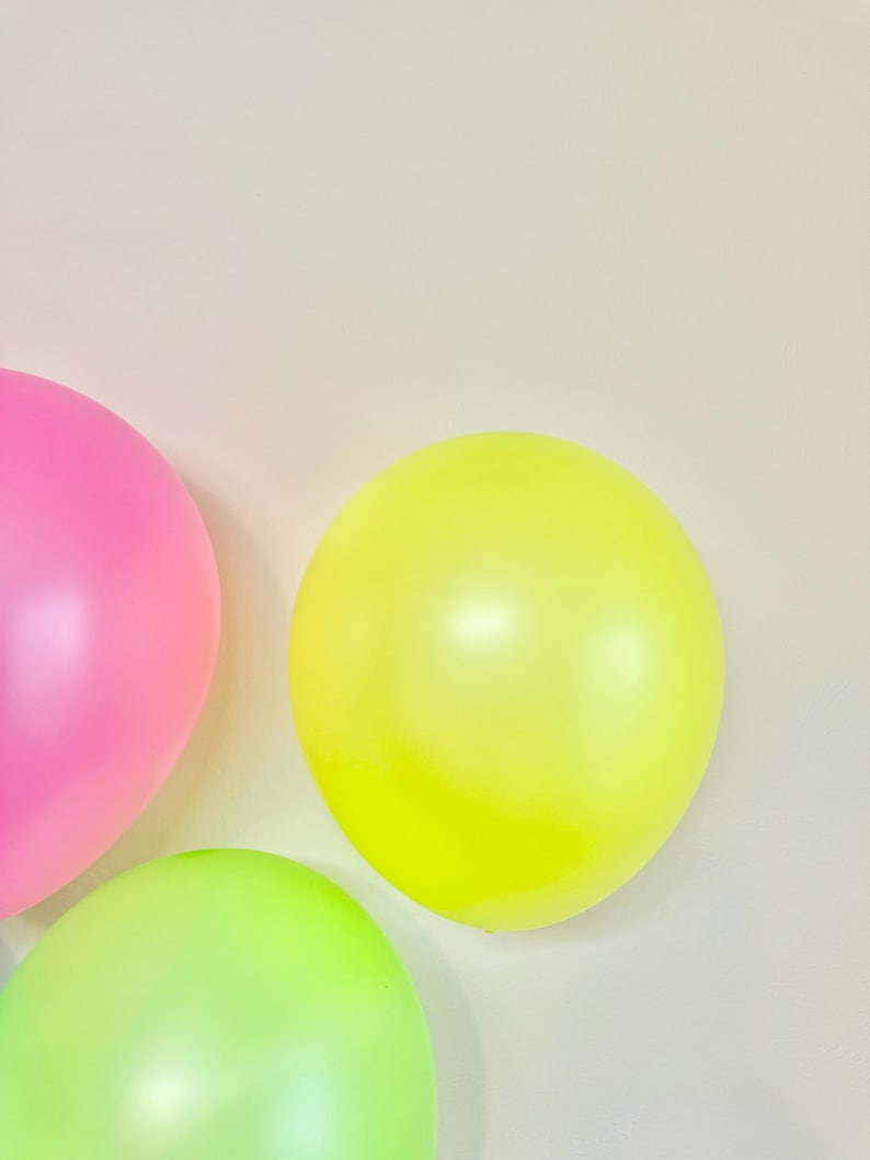 May include: Three balloons in different colours: pink, yellow and green. The balloons are against a white background.