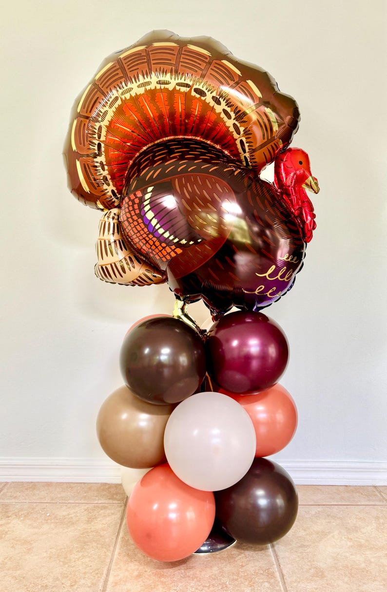 May include: A brown and gold turkey balloon with a red head and wattle, surrounded by a cluster of brown, burgundy, beige, and peach balloons.