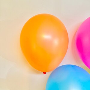 May include: Three balloons, one orange, one pink, and one blue, against a white background.