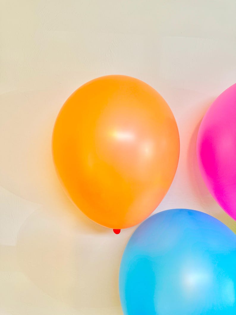 May include: Three balloons, one orange, one pink, and one blue, against a white background.