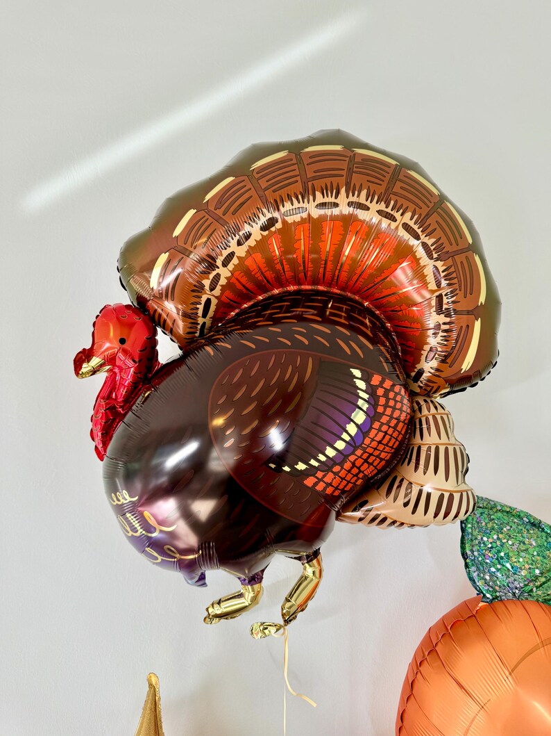 Puede incluir: Un globo de aluminio de color marr&oacute;n y dorado con forma de pavo con cabeza y barbilla rojas. El pavo tiene un dise&ntilde;o detallado de plumas en su cuerpo y cola.