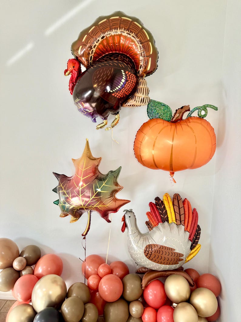 Puede incluir: Un arreglo de globos con tem&aacute;tica de Acci&oacute;n de Gracias con un globo de pavo marr&oacute;n y naranja, un globo de calabaza naranja grande, un globo de hoja roja y dorada y un globo de pavo gris y marr&oacute;n. Los globos est&aacute;n rodeados de una variedad de globos m&aacute;s peque&ntilde;os en tonos marrones, dorados y rojos.