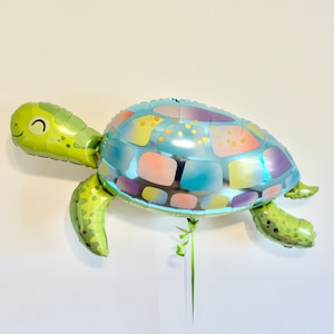 May include: A turtle-shaped foil balloon in shades of green, blue, and pastel colors. The balloon has a smiling face and is designed to resemble a sea turtle. It is suspended by a green ribbon.