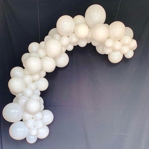 May include: A white balloon arch, made of many white balloons of different sizes, arranged in a curved shape.