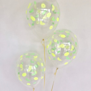 K&ouml;nnte beinhalten: Drei transparente Ballons mit Zitronen- und Blattmotiven. Die Ballons sind mit goldenen B&auml;ndern gebunden.