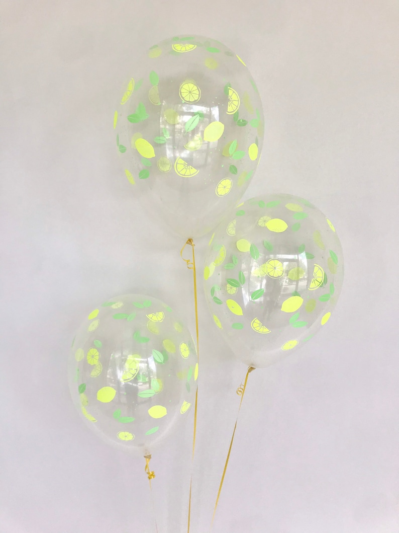K&ouml;nnte beinhalten: Drei transparente Ballons mit Zitronen- und Blattmotiven. Die Ballons sind mit goldenen B&auml;ndern gebunden.