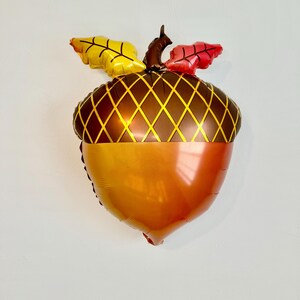 Pu&ograve; includere: Un palloncino di alluminio a forma di ghianda di colore marrone e arancione con foglie gialle e rosse in cima.
