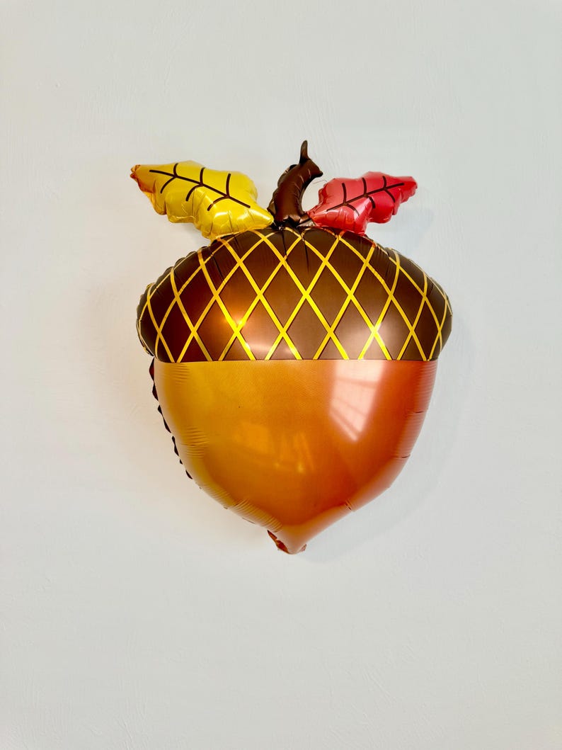 Pu&ograve; includere: Un palloncino di alluminio a forma di ghianda di colore marrone e arancione con foglie gialle e rosse in cima.