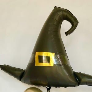 May include: A green witch hat balloon with a gold buckle. The balloon is shaped like a pointed hat with a curled brim.