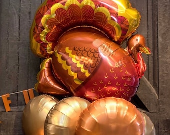 May include: A large, gold and red foil balloon shaped like a turkey. The balloon is surrounded by smaller, gold and copper foil balloons.