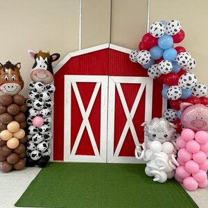 K&ouml;nnte beinhalten: Ein roter Scheunenhintergrund mit Ballontierdekorationen f&uuml;r eine Bauernhof-Mottoparty. Die Dekorationen umfassen ein braunes Pferd, eine schwarz-wei&szlig;e Kuh, ein wei&szlig;es Lamm und ein rosa Schwein.