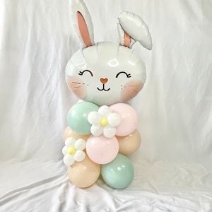 May include: A white bunny balloon with pink ears and a smiling face, surrounded by pastel green, pink, and beige balloons with white flowers.